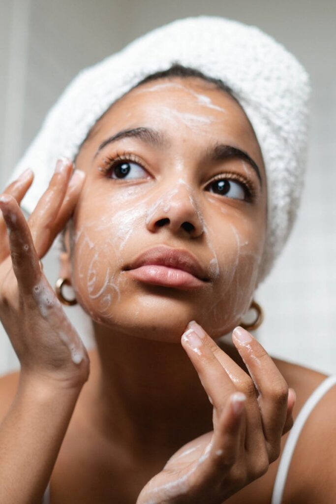 A young woman applies skincare cream in a modern bathroom setting.
